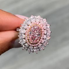 a close up of a person's hand holding a ring with a pink and white diamond