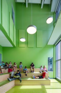 children are sitting on the stairs in an open room with bright green walls and flooring