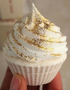 a hand holding a cupcake with white frosting and gold sprinkles