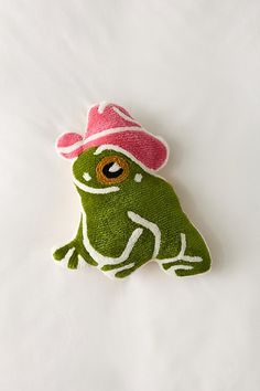 a green frog with a pink hat on it's head sitting on a white sheet