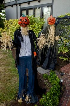 two scarecrows are standing in front of a house with pumpkin heads on their heads