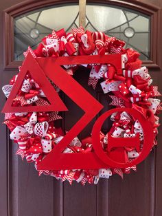 a red wreath with the letter g on it is hanging from a front door decorated with bows and ribbons