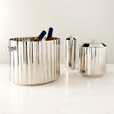 three stainless steel containers with wine bottles in them on a white countertop next to each other