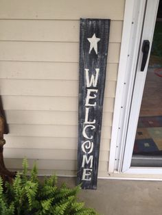 a welcome sign on the side of a house next to a potted plant and door