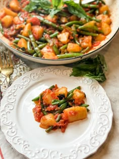 a white plate topped with food next to a pan filled with green beans and potatoes