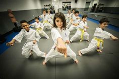 a group of kids in white uniforms doing karate moves on a black mat with their arms stretched out