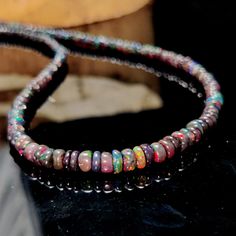 two bracelets with multicolored beads sitting on top of a black table next to a piece of wood