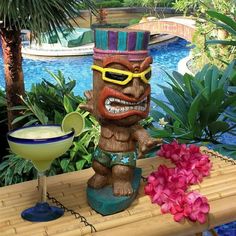 a tiki statue sitting next to a cocktail glass on a table near a pool