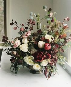 a vase filled with lots of flowers sitting on top of a table next to a window