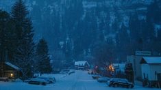 cars parked on the side of a snowy road in front of a mountain with snow covered trees