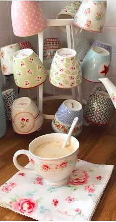 a cup of coffee sitting on top of a wooden table next to cups and saucers