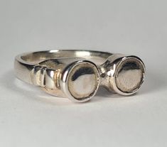 **Please note that we dispatch on Tuesdays unless special delivery express option is paid for** Sterling silver 'Goggles' ring. Original design carved in wax then lost wax cast into solid recycled sterling silver.  Designed and made in London.   Finish options: - Silver (brightly polished) - Oxidised (It's still silver, but a blackened finish is applied all over the ring and then buffed *mostly* away, leaving the recessed details darker and more pronounced - Engraved (The words you enter in the personalisation box will be engraved by hand on the inside of the ring in cursive style unless you request otherwise) - Gem set (gems will be set into the centre of each goggle lens. Please let us know your preferred gem colour in the personalisation box. PLEASE NOTE: Adding gems to your ring will e Antique Sterling Silver Hand Cast Rings, Vintage Hand Cast Sterling Silver Signet Ring, Antique Hand Cast Sterling Silver Rings, Hand-cast Vintage Engraved Ring, Vintage Hand Cast Engraved Round Ring, Vintage Silver Hand Cast Ring, Antique Hand Cast Silver Rings, Vintage Silver Rings With Hand Cast Design, Hand Cast Sterling Silver Engraved Ring