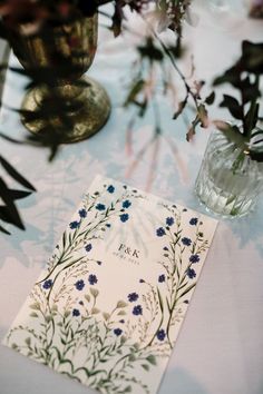 a table with blue flowers in vases and a white card on top of it