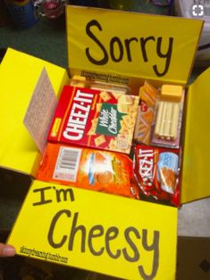 a person holding up a yellow box filled with snacks and candy that reads sorry, i'm cheesy