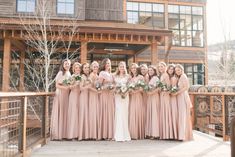 a group of women standing next to each other in front of a wooden building holding bouquets