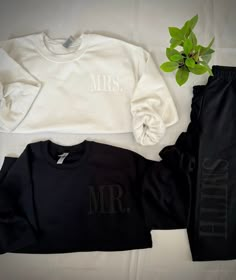 two personalized sweatshirts and sweatpants are laid out next to a potted plant