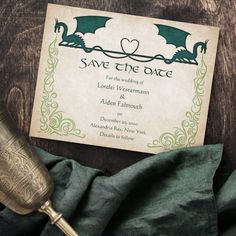 an ornate save the date card next to a wine glass and a golden cup on a wooden table