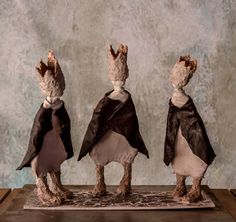 three small figurines wearing capes on top of a table