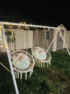 two hanging chairs with lights on them in the grass next to a shed at night