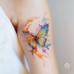 a colorful butterfly tattoo on the right arm and shoulder, with watercolor splashs