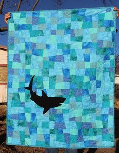 a person holding up a blue quilt with a black shark on it's side