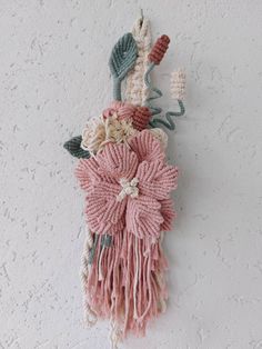 a wall hanging made out of yarn with flowers and leaves on the top, attached to a white wall