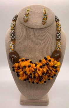 This beautiful safari statement necklace is handmade in Accra, Ghana using hand-made animal print powdered glass beads with large glass beads on either end of a nest of yellow/ orange medium beads crowned sporadically with small black beads. This gorgeous necklace will adorn you beautifully. Materials: small beads, GIVE, glass beads, LOVE, handmade beads, HOPE, silver toned lobster clasp. Necklace extenders are included for a longer look if the necklace fastener is compatible. Earrings are also included. Necklace length: 17" Unique Orange Jewelry With Wooden Beads, Orange Wooden Beads For Jewelry Making, Handmade Orange Resin Necklace, Orange Necklace With Black Round Beads, Unique Orange Resin Jewelry, Unique Polished Orange Beads, Orange Beaded Costume Jewelry Necklaces, Unique Yellow Beads For Jewelry Making, Unique Yellow Wooden Beads