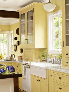 a kitchen with yellow cabinets and white counter tops is pictured in this image, there are two windows above the sink