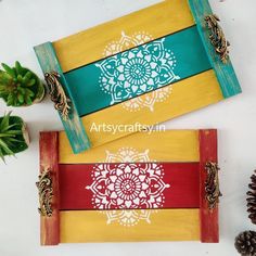 two painted wooden trays with pine cones and succulents next to each other