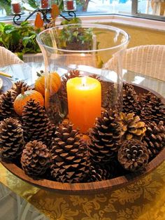 pine cones and oranges are arranged around a lit candle on a glass table with wicker chairs in the background