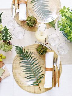 the table is set with plates, silverware and green plants