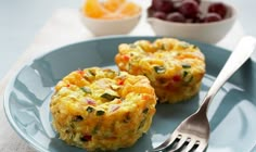 two muffins on a plate with a fork and bowl of fruit in the background