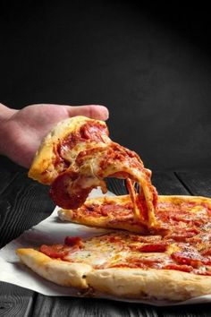 a person taking a slice of pizza from a paper plate on a wooden table with black background