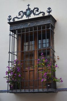 a window with bars and flowers on the outside, in front of a white building