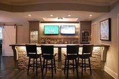 a bar with four stools in front of it and two television screens on the wall