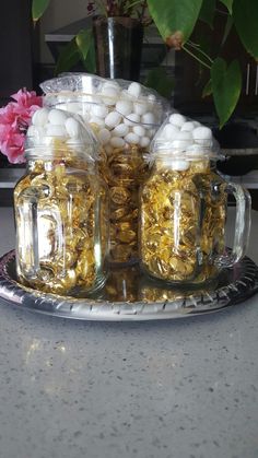 two mason jars filled with gold and white candies sitting on a silver platter