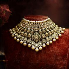 an elaborate necklace with pearls and stones on display in front of a red velvet case