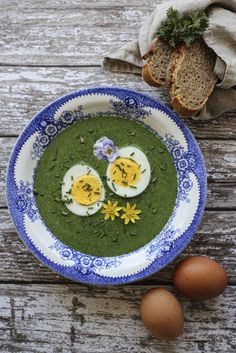 two eggs are on top of green soup in a blue and white bowl next to some bread