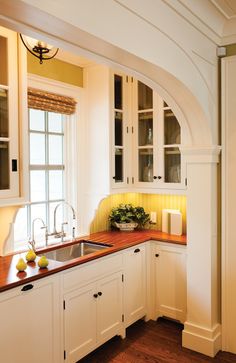 a kitchen with white cabinets and wooden counter tops, along with an arched window over the sink