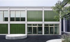 the building has many windows and green shutters on it's sides, as well as a circular concrete bench in front