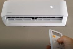 a person holding a remote control in front of an air conditioner that is on top of a table