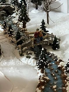 a toy train set is shown in the snow with trees and water running through it