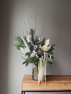 a vase filled with white flowers on top of a wooden table next to a gray wall