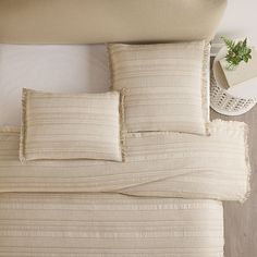 a close up of a bed with pillows and blankets on top of it, next to a night stand