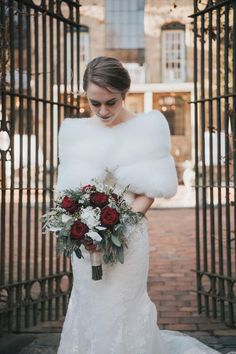 a woman in a wedding dress holding a bouquet and fur stoler over her shoulder