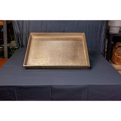 a square metal tray sitting on top of a blue table cloth covered table with other items in the background