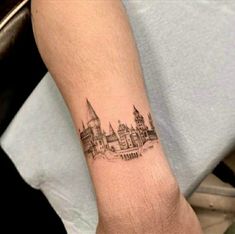 a tattoo on the arm of a person with a castle in the background and buildings behind it