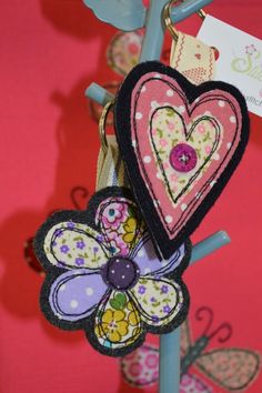 two heart shaped brooches hanging from a blue pole with pink and yellow flowers