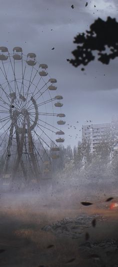 a ferris wheel in the middle of a field with trees and buildings behind it on a foggy day