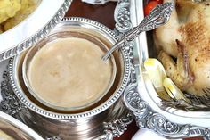 a silver plate topped with chicken next to a bowl filled with gravy and other food